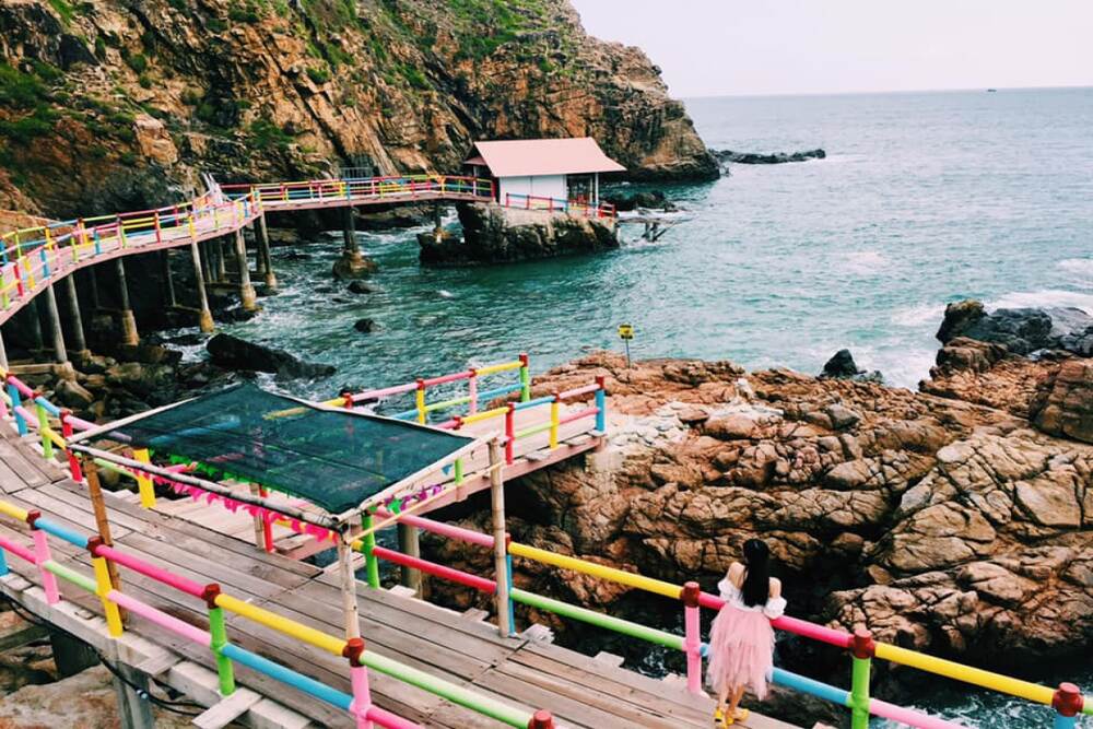 On Kỳ Co beach, Cầu Hang Yến emerges as a graceful accent, a small wooden bridge curving out into th...